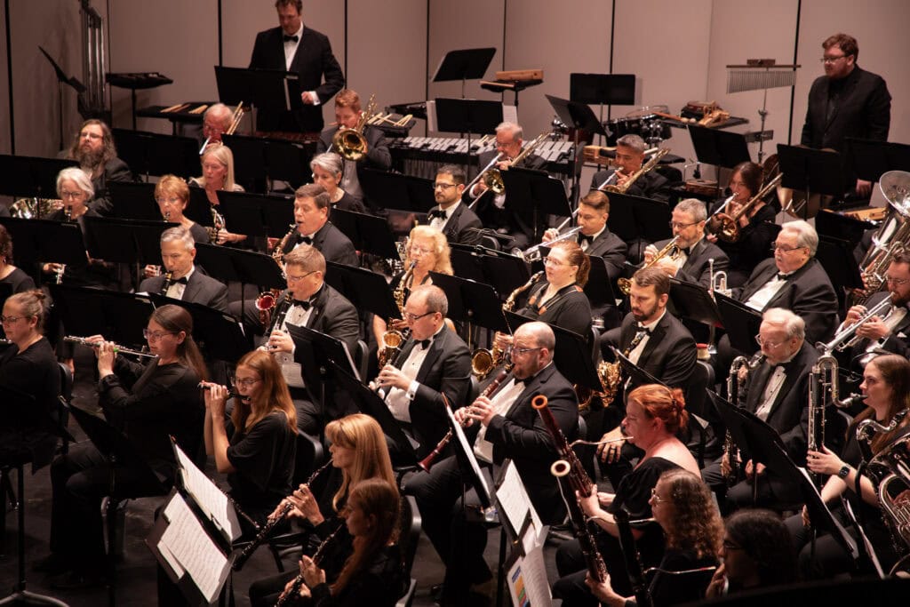 Large orchestra performing at a concert with various instruments and musicians.